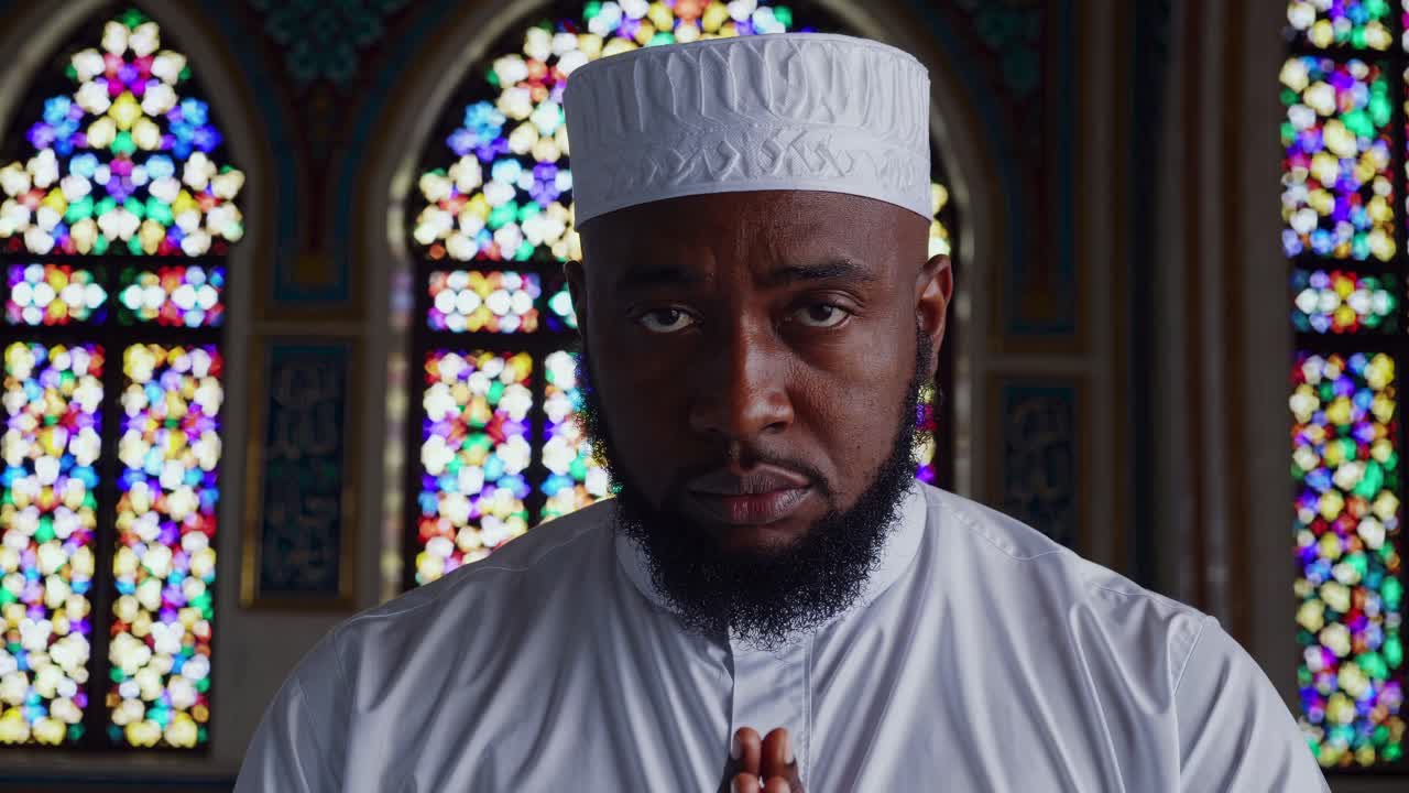 Video seorang pria dengan pakaian tradisional berdoa di masjid, dengan jendela kaca patri berwarna-warni