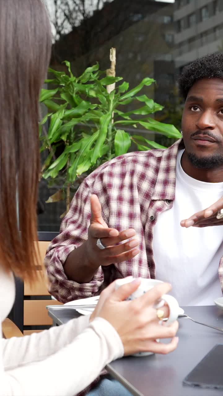 Young Man Gesturing While Talking to a Woman at a Cafe