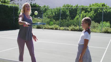 caucasian mother teaching her daughter to play tennis at tennis court on a bright sunny day