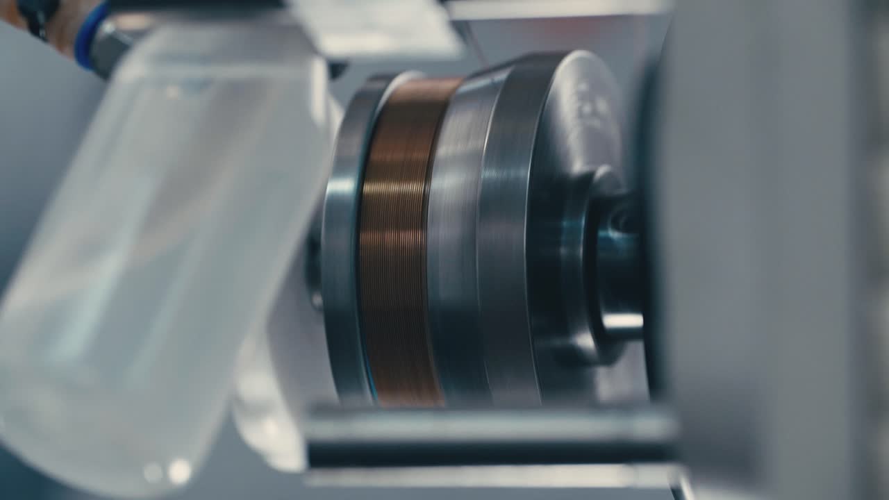 Factory machinery spinning in slow motion, copper wire being coiled by the machine, showcasing modern manufacturing technology
