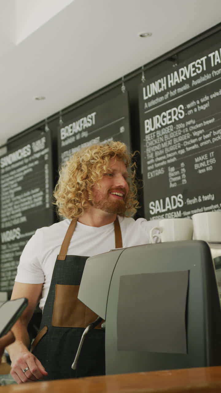 Vertical video of happy diverse male barista and woman paying with smartphone for coffee in cafe