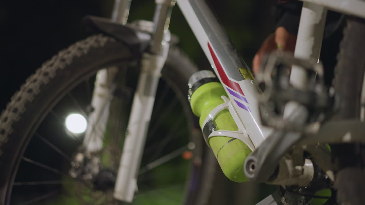 Motorcycle With Bottle, Close View Of White Bike Featuring Green Bottle In Night Scene, Low Angle Shot Of Stationary Bicycle With Bottle Beneath Frame In Tranquil Outdoor Nighttime Setting