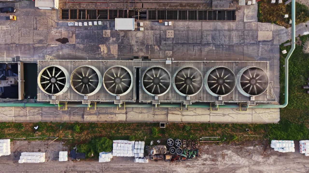 Cooling fans are seen on top of a large industrial building during daylight in an outdoor setting