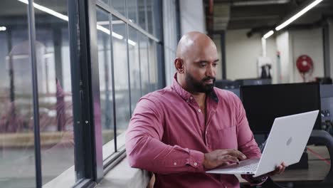 happy biracial male creative using laptop at casual office, in slow motion