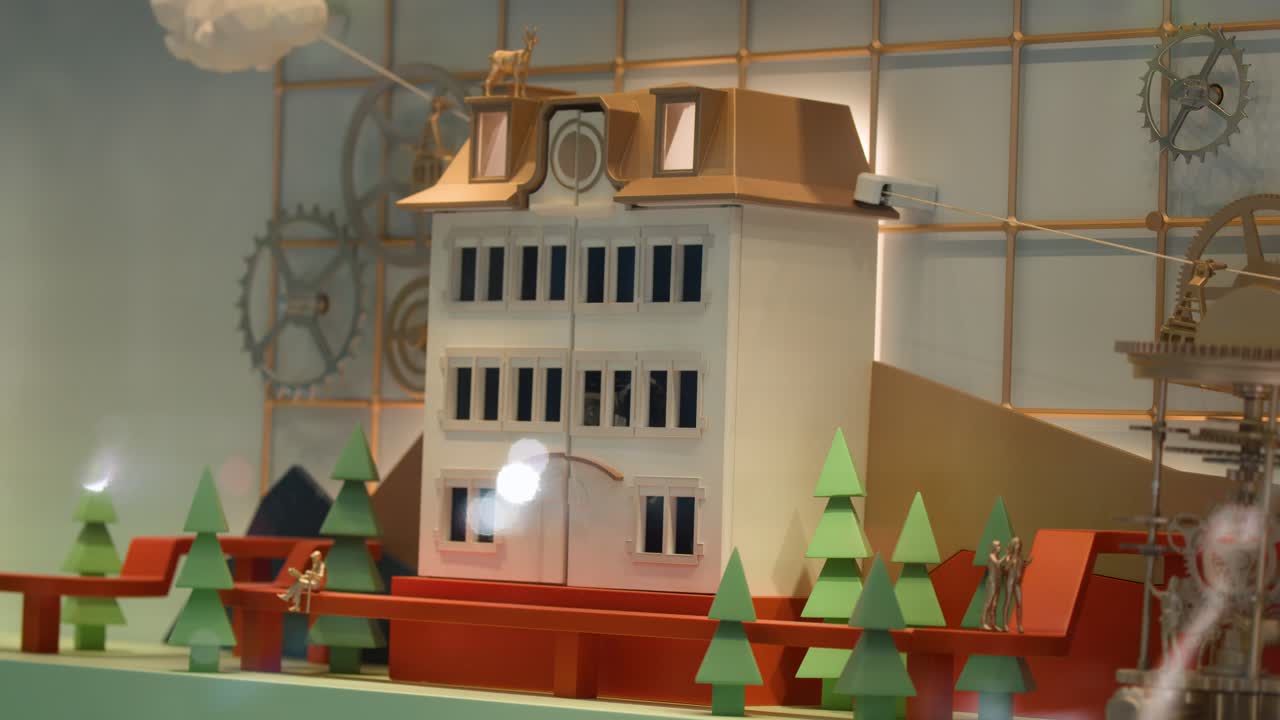 Miniature building facade opens mechanically, revealing intricate clockwork in a brightly lit showcase