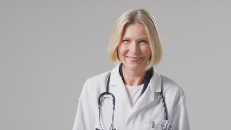 retrato de estudio de una doctora madura con estetoscopio con abrigo blanco contra un fondo plano