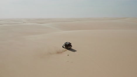 Aerial:-A-truck-with-kitesurfers-traveling-through-the-dunes-of-Lencois-Maranhenses-in-Brazil,-during-dry-season