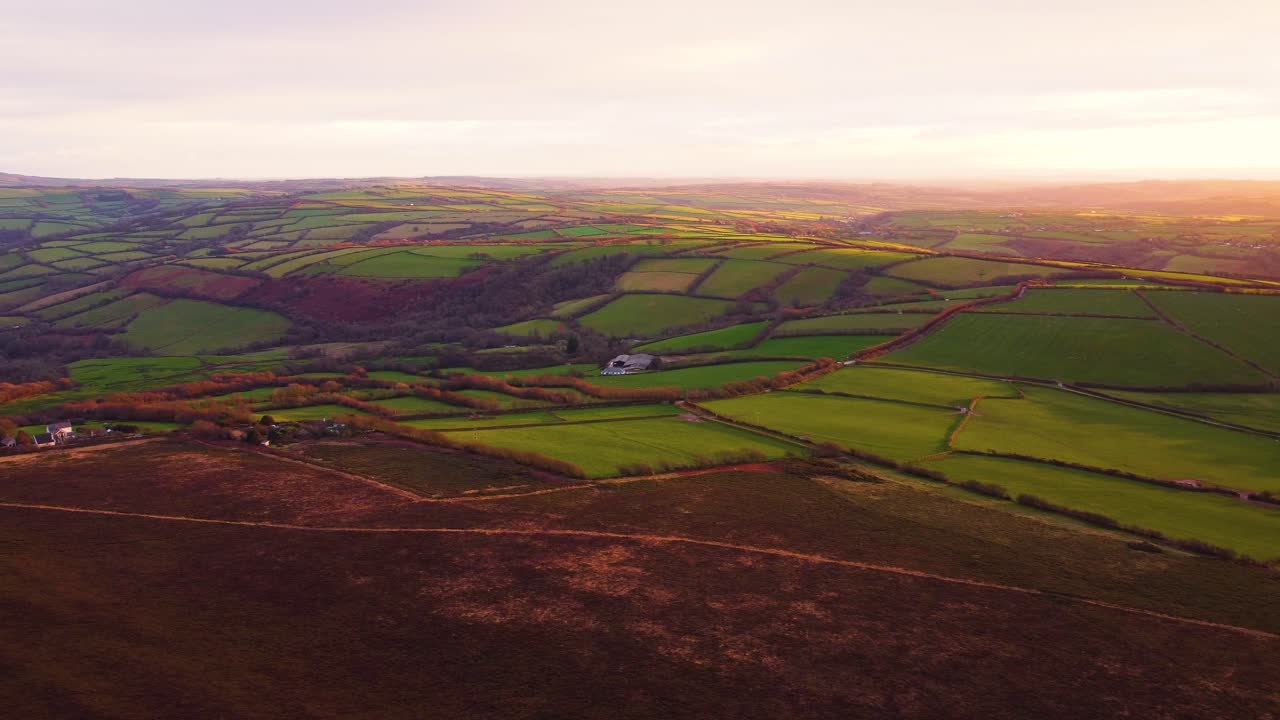 Droneflyvning ved solnedgang over fredfyldt Devon-landskab med gyldent sollys, der skaber dybe skygger hen over markerne. Perfekt til rejsedokumentarer, naturfilm og etableringsbilleder.