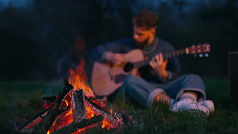 man sits by fire playing the guitar. man with guitar resting near bonfire outdoors at night