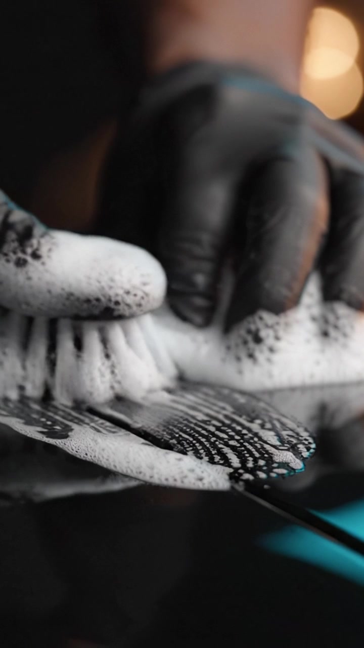 A close-up view of a person using a brush to clean a surface, showcasing the sudsy foam and attention to detail in the cleaning process.