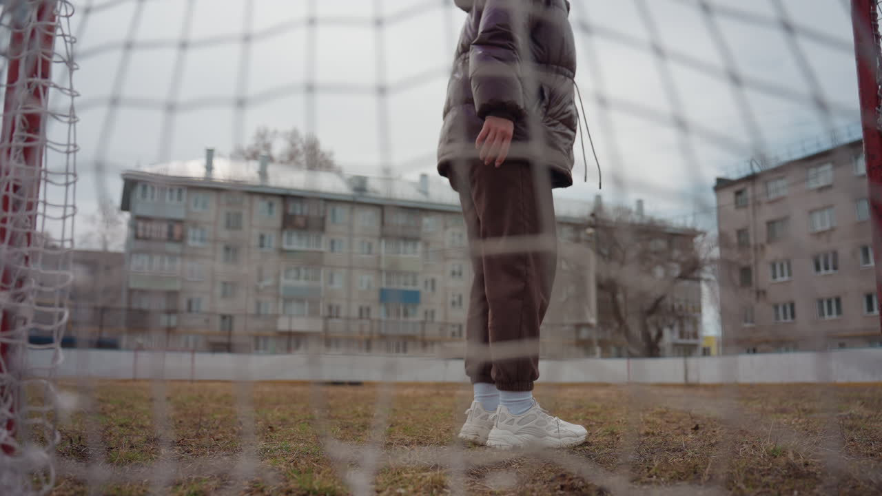 도심 피치에서 근거리 슛을 막는 흰색 유니폼의 골키퍼, 낮은 네트 시점, 긴장된 다리와 집중된 자세, 배경에는 아파트 단지, 투박한 길거리 축구 분위기