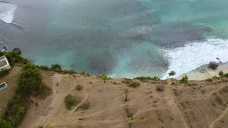 Fly-drone-backward-above-Indian-Ocean-filming-big-waves-and-Dreamland-beach-hill-in-Bali-Indonesia