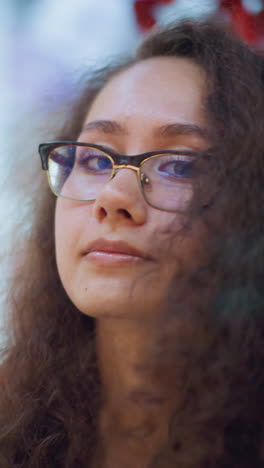hermosa dama con el cabello rizado en un centro comercial bien iluminado, ajustando el cabello hacia atrás con una sonrisa suave, mostrando sus uñas fijas, brazalete de muñeca y reloj inteligente, el fondo destaca el vibrante ambiente interior