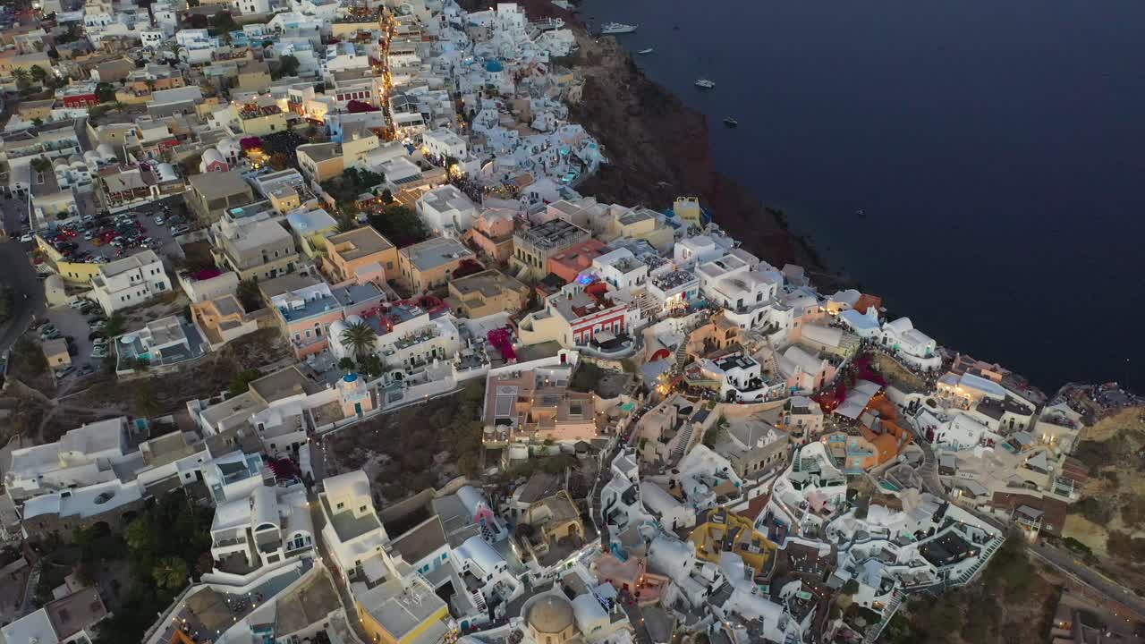 Oia white cave houses and villas top down view from drone spinning during sunset in Santorini, Greece.