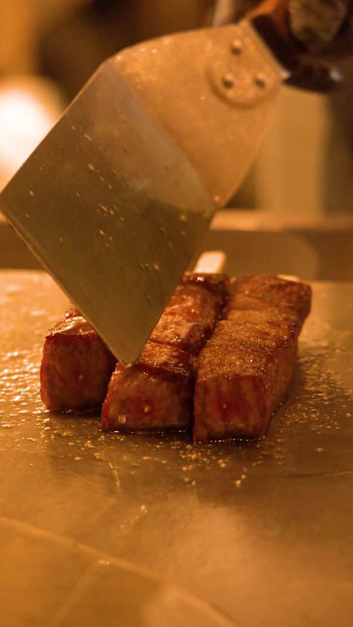 Primo piano di uno chef che usa una spatola per pressare spiedini di manzo wagyu conditi su una piastra