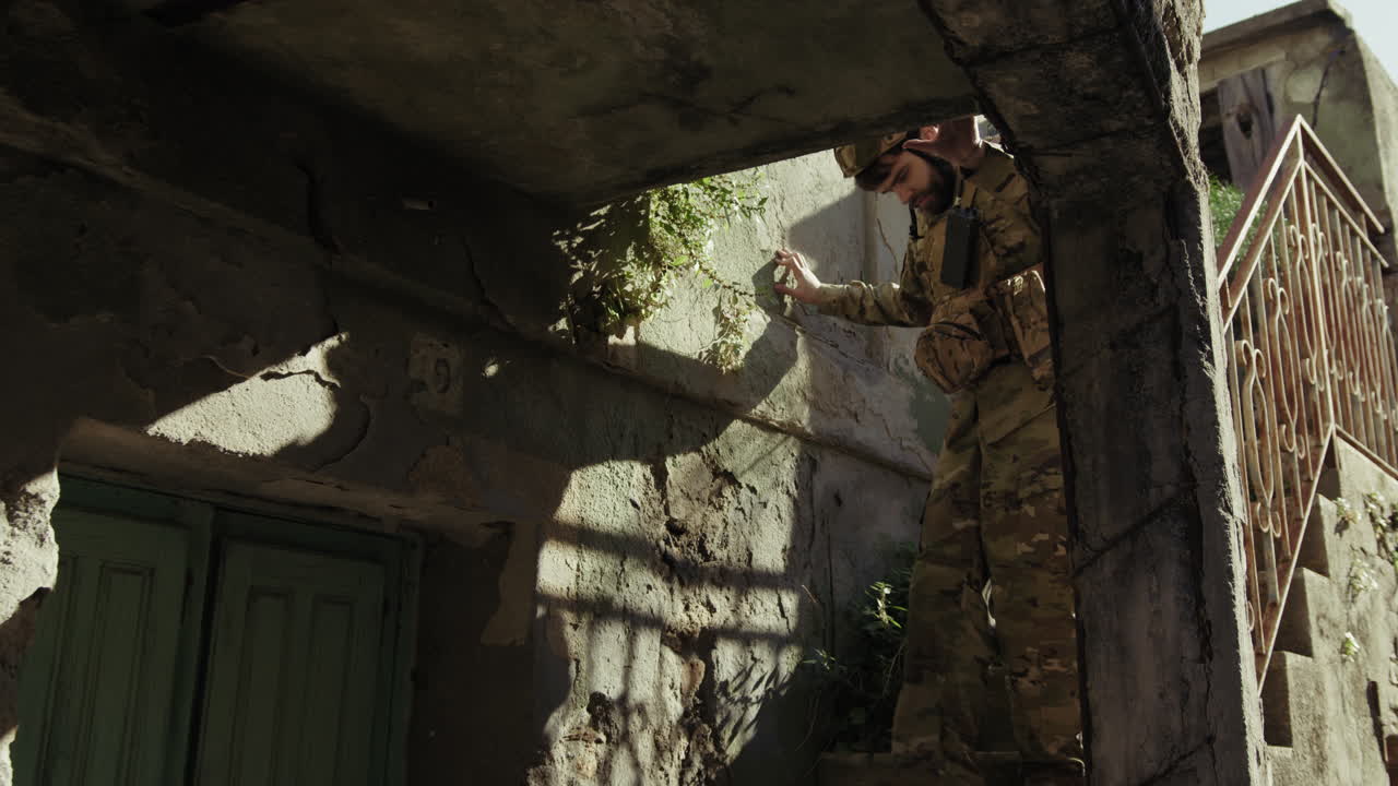 Un giovane soldato scende con cautela le scale di una casa distrutta.