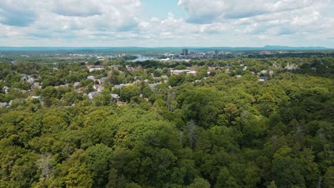 Eine-Wunderschöne-Drohnenaufnahme-Eines-Grünen-Waldes-In-Der-Nähe-Einer-Stadt,-In-Deren-Mitte-Sich-Ein-See-Befindet