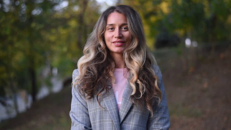 Primer plano de una mujer rubia con una americana gris sonriendo a la cámara en el parque