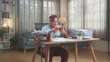hombre gordo asiático jugando al juego en el teléfono inteligente después de trabajar con documentos en la oficina