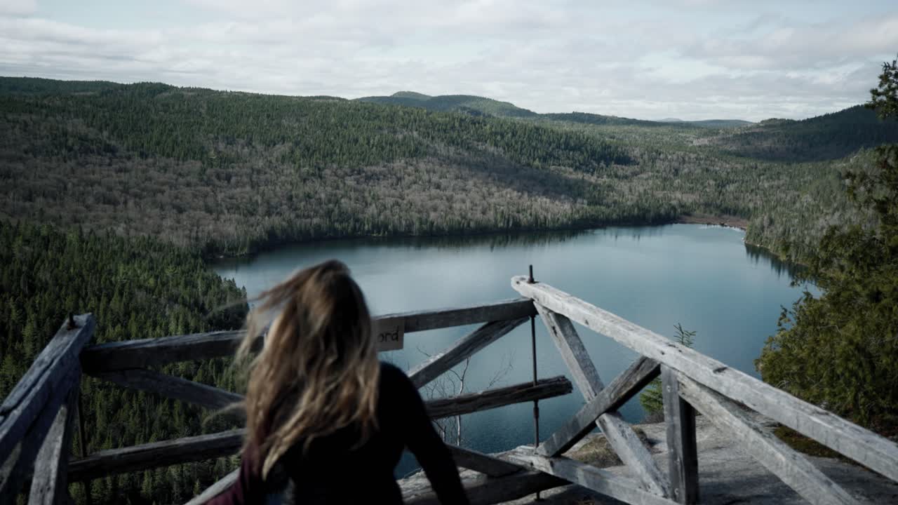 turista caucásica de pie en un balcón de madera elevado con vistas al hermoso lago en saint-come, quebec, canadá