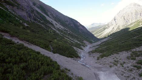 imágenes aéreas de drones volando a lo largo de las laderas de las montañas a través de un espectacular valle glacial rodeado de pinos con parches de nieve y un río alpino en suiza