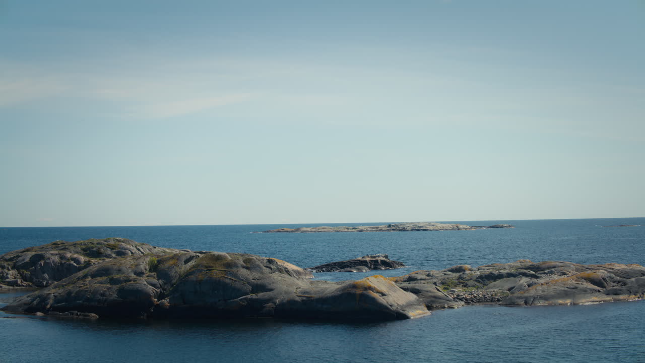 Slow motion wide shot of the blue water and rocks in Raet National Park, Norway. Small waves ripple across the water, filmed on a bright sunny day