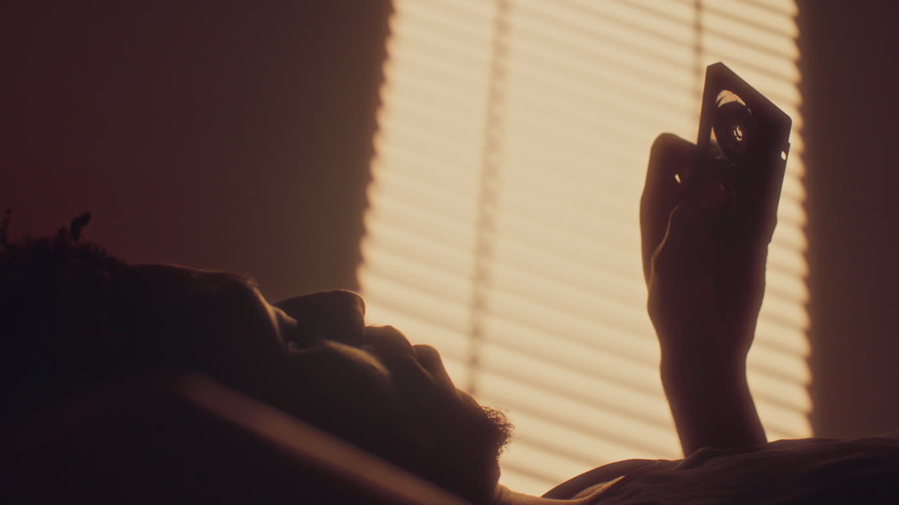 African American Man Resting on Bed and Looking at Cassette Tape