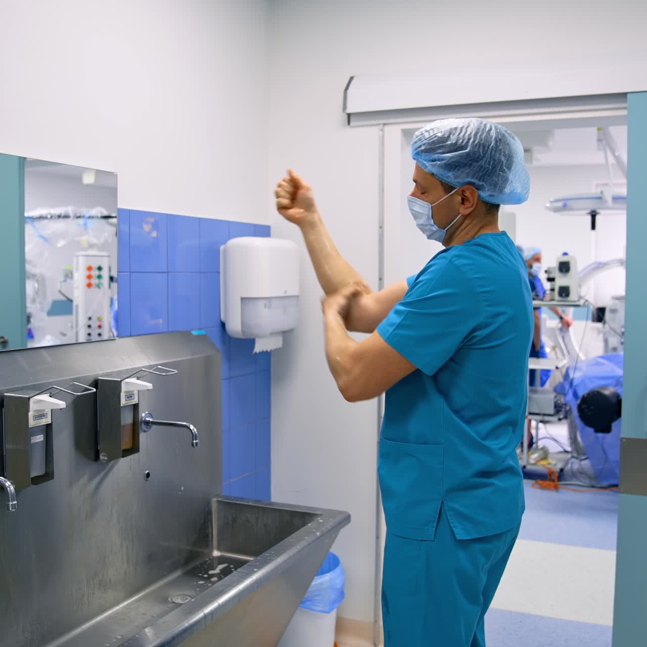 Un medico uomo si prepara attentamente per l'operazione. Un chirurgo in uniforme blu applica del disinfettante sulle mani e lo strofina accuratamente.
