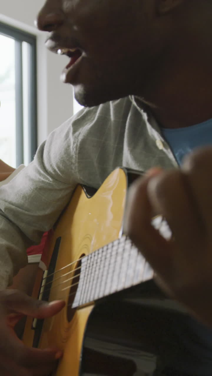 video de una feliz pareja afroamericana sentada en el sofá, cantando y tocando la guitarra