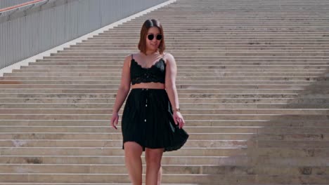 Female-Wearing-Sunglasses-In-Black-Summer-Outfit-Casually-Walking-Down-Stairs-And-Twirling-In-Valletta,-Malta