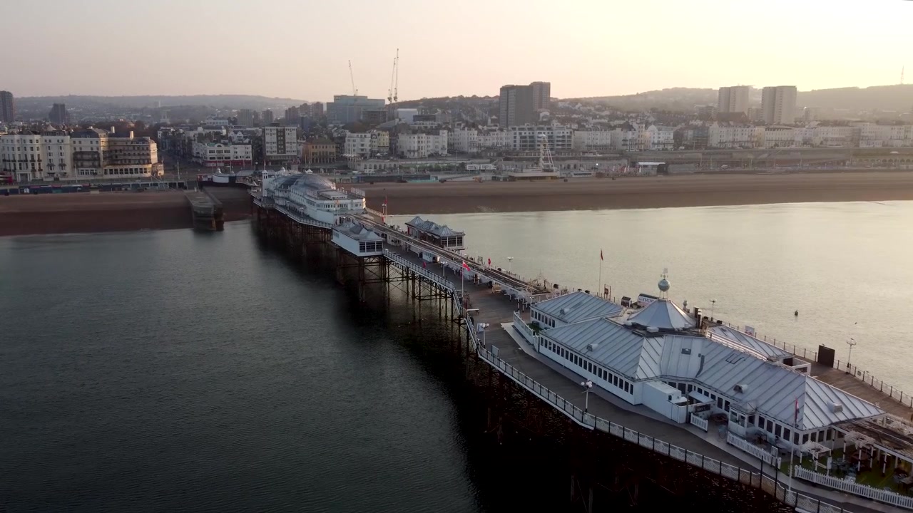 Ripresa con drone del sole che sorge su un paesaggio urbano e un molo che si estende nel mare