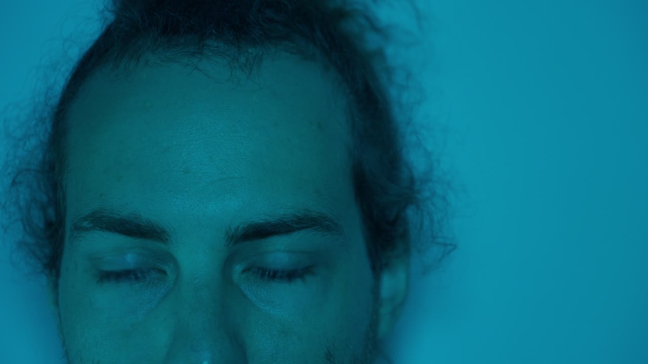 Moody portrait of a worried man with blue lighting, showing his contemplative gaze as eyes swing side to side