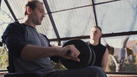 side view of a disabled man in wheelchair and his personal trainer working out with dumbbell at home