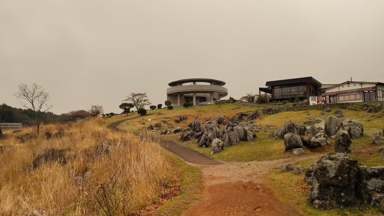 Slow push-in shot along a path towards the Akiyoshidai observatory. The unique karst landscape with its limestone rocks and autumn grass is shrouded in moody, atmospheric fog.