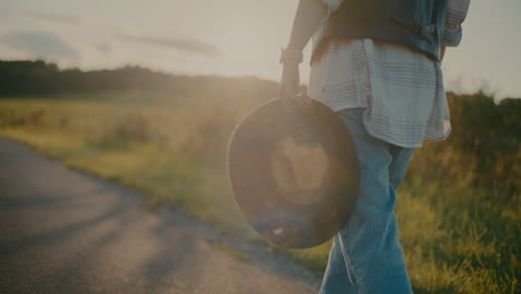 woman holding hat while strolling near meadow