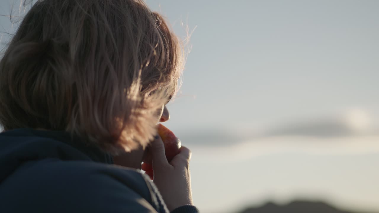 mujer rubia con gafas de sol comiendo manzana en la luz del sol de la hora dorada