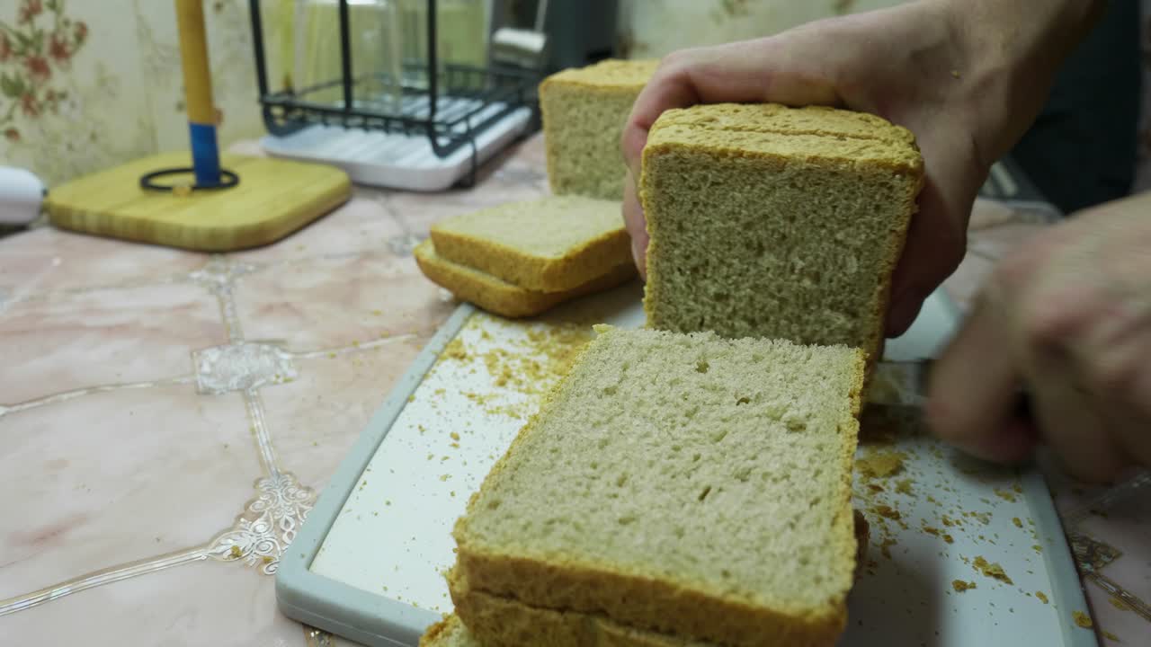 Se corta pan recién hecho sobre una tabla de cortar. Se ven unas manos que muestran una tarea de cocina sencilla y cotidiana.