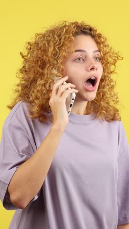 woman with curly hair reacts with shock while on a phone call