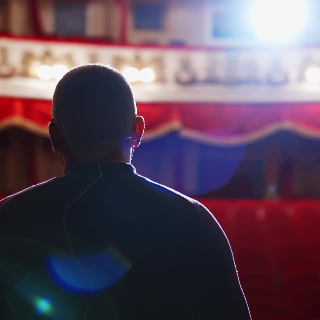 Actor rehearsing in front of empty auditorium. Back view of a man on stage against spotlight in the theater. Male performer speaking on scene. Close-up