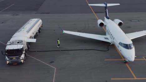 private jet getting fueled up by aviation fuel truck on airport tarmac, aerial