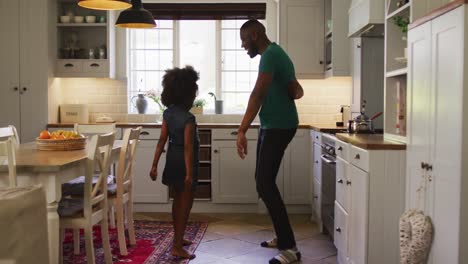 african american daughter and her father dancing together in kitchen