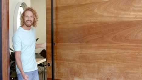 portrait of happy caucasian man at home opening front door and beckoning in slow motion