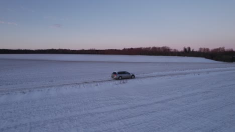 El-Coche-Conduce-Por-Una-Carretera-Cubierta-De-Nieve-Helada-En-Dinamarca,-El-Dron-Escandinavo-Vuela-Junto-A-Un-Coche-Que-Conduce-Por-Una-Carretera-Helada-Con-Nieve-Que-Cubre-Los-Campos-Con-Un-Profundo-Manto-De-Nieve