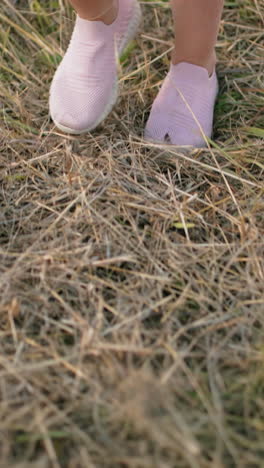 primer plano de una persona caminando por un campo de hierba seca con zapatillas de deporte rosadas, los pasos se mueven naturalmente sobre un terreno desigual con una mezcla de hierba verde y amarilla