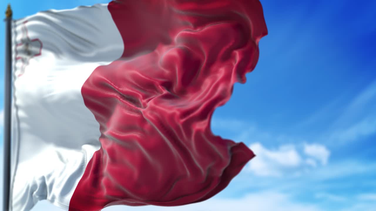 la bandera maltesa está ondeando lentamente contra el cielo azul.