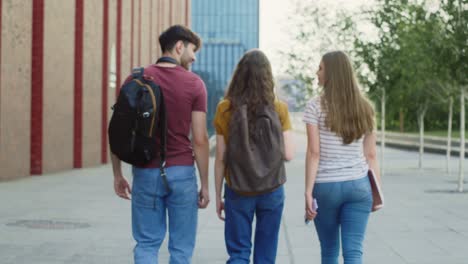 Zoom-out-of-back-view-of-three-caucasian-students-walking-through-university-campus