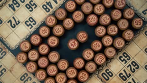 primer plano cinematográfico suave disparo desde arriba de una pila de barriles de madera de bingo en un cuadrado, figuras de madera, viejos números de fondo, juego de mesa vintage, cámara lenta 120 fps comercial zoom giratorio en