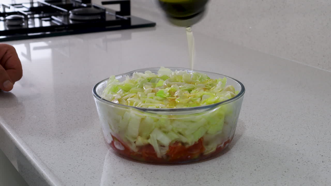 Close-up of fresh cabbage and tomato salad in a glass bowl as olive oil is being poured on top, highlighting healthy eating and freshness