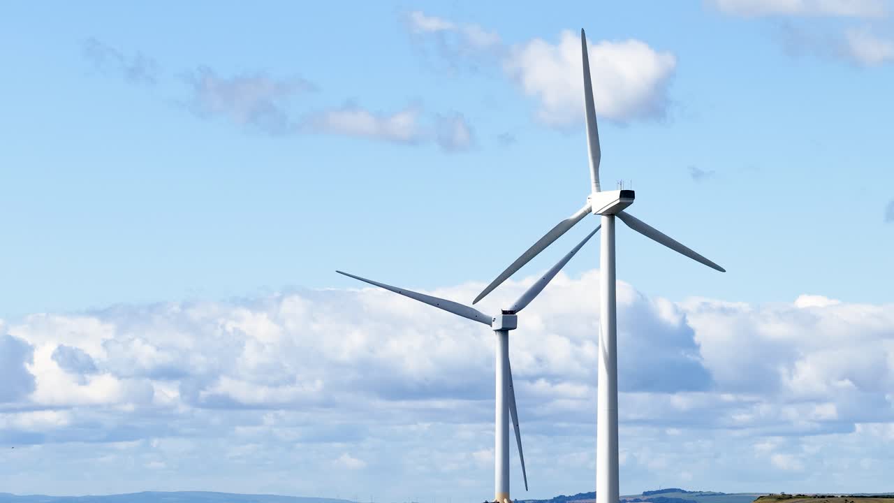 Two wind turbines spin steadily under bright daylight, wide shot, clear sky, coastal landscape