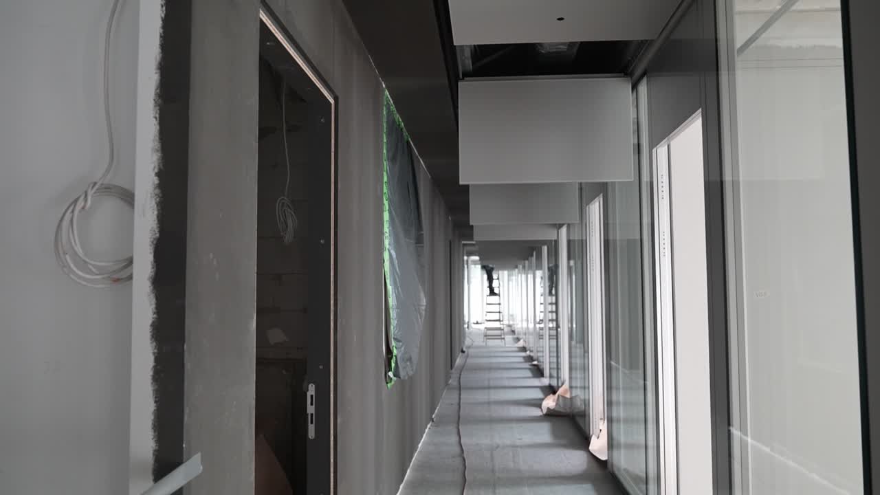 Corredor interior con paneles de techo y paredes de cristal en un edificio sin terminar, espacio de arquitectura moderna durante la fase de acondicionamiento con elementos de techo suspendidos y perspectiva lineal.